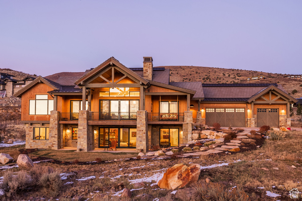View of front facade featuring a balcony, stone siding, a chimney, and a garage