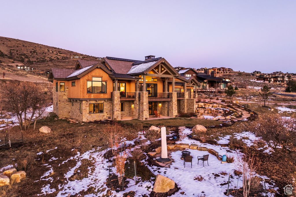 Snow covered rear of property with a balcony, a chimney, a fire pit, and a tile roof