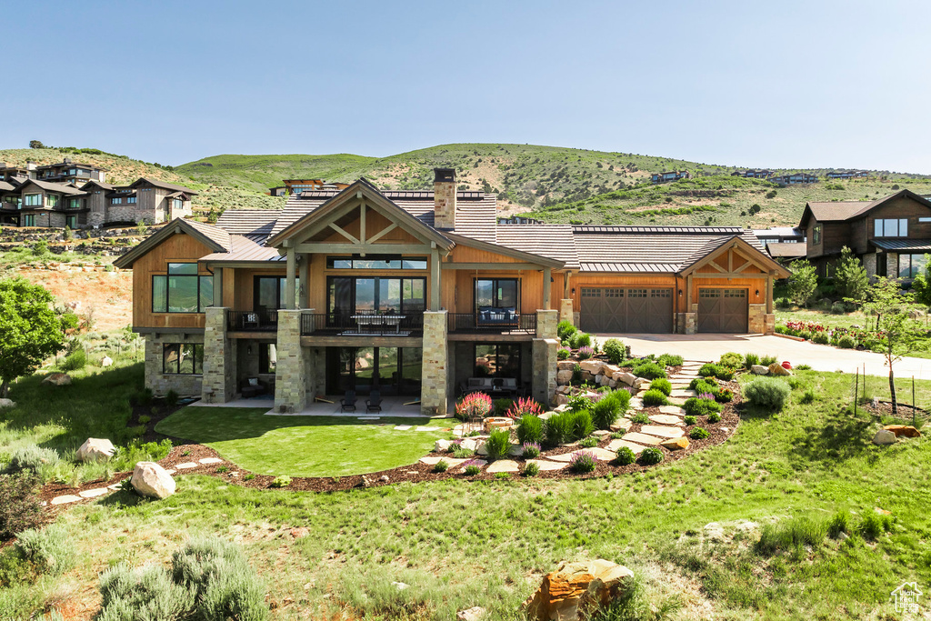 View of front of house with a balcony, stone siding, a chimney, a mountain view, and concrete driveway