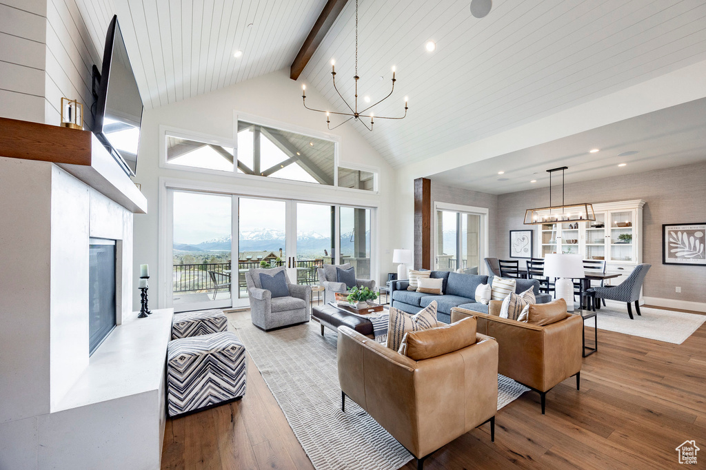 Living room with a chandelier, beamed ceiling, hardwood / wood-style flooring, a glass covered fireplace, and high vaulted ceiling