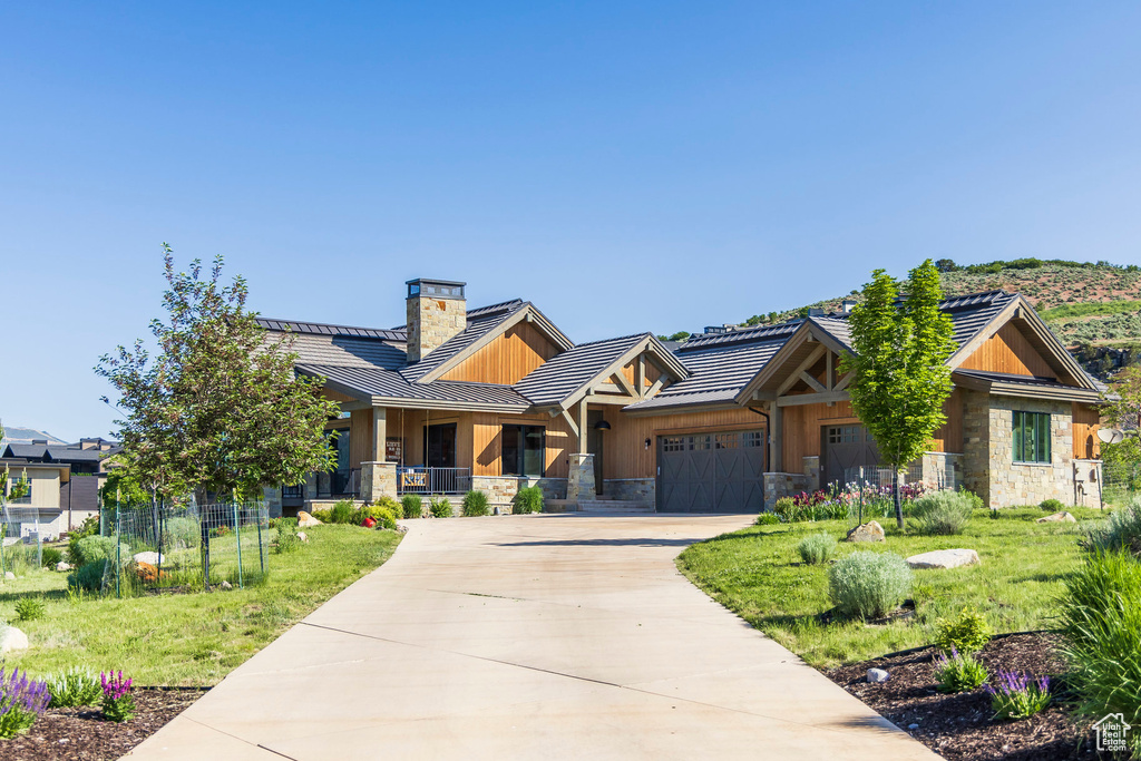 View of front of home with driveway, stone siding, a chimney, an attached garage, and a tiled roof