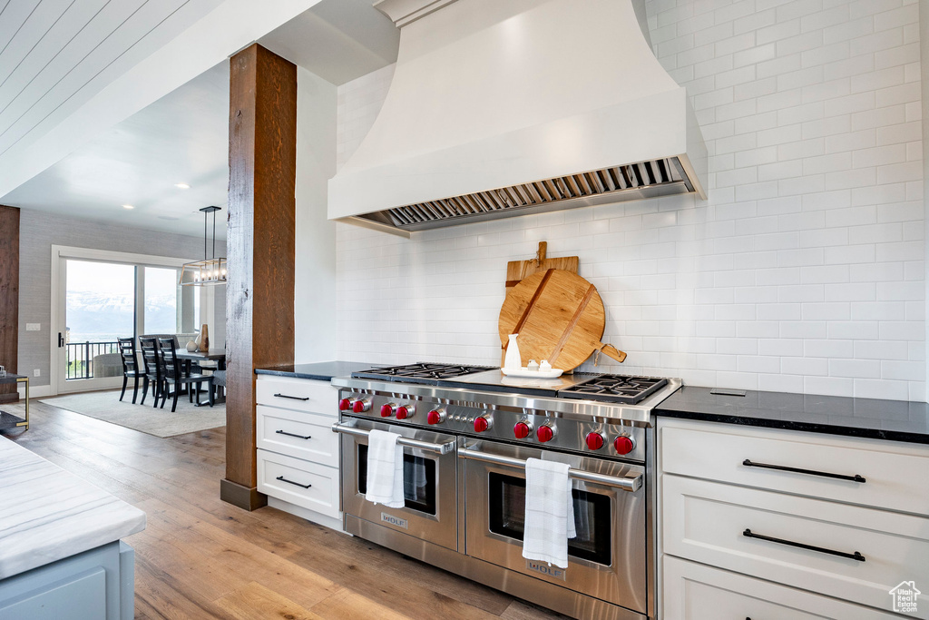 Kitchen featuring custom range hood, double oven range, tasteful backsplash, light wood finished floors, and a chandelier