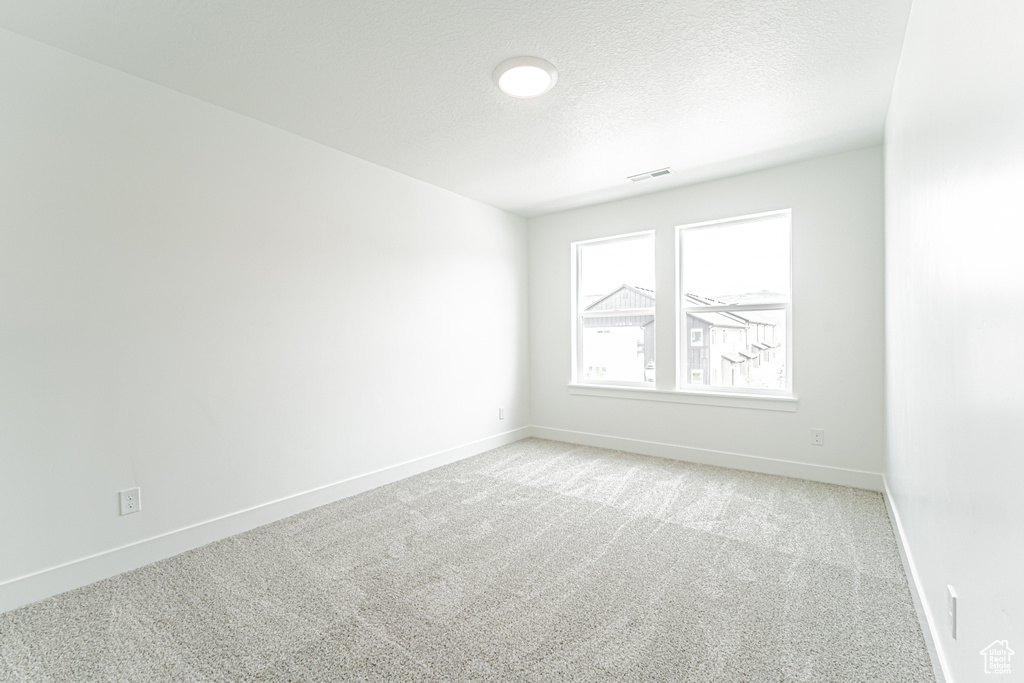 Empty room featuring light colored carpet and a textured ceiling