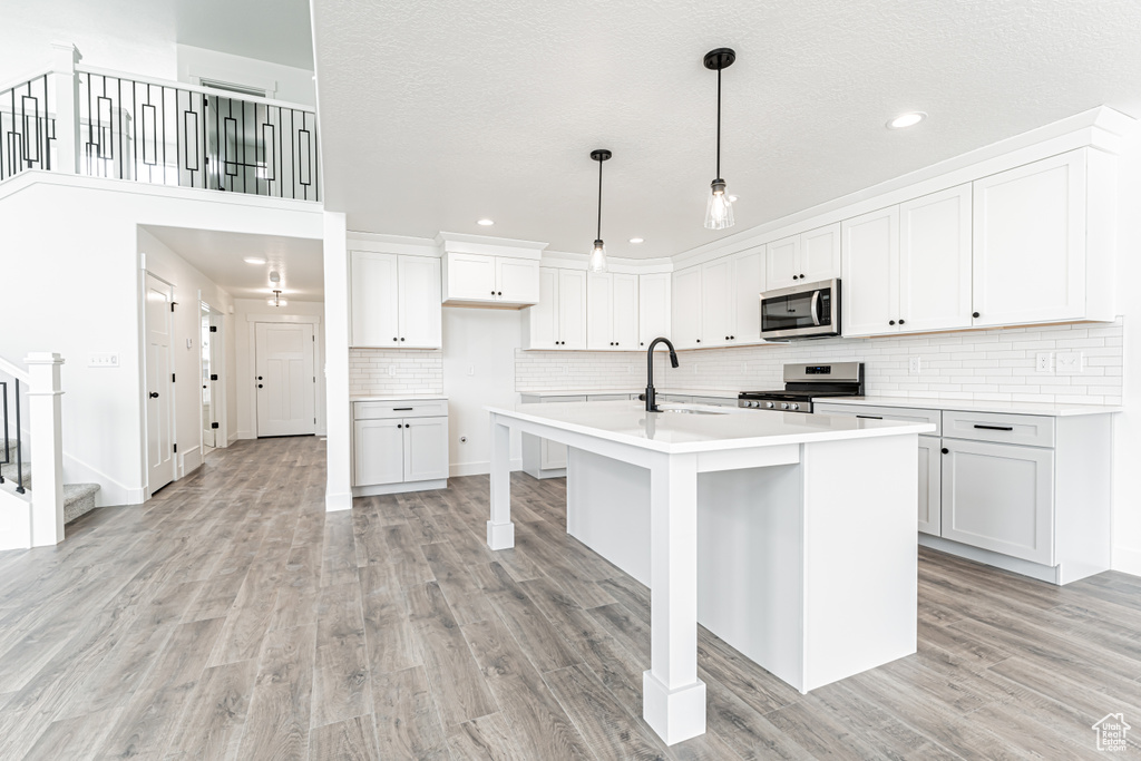 Kitchen with appliances with stainless steel finishes, light wood-style flooring, recessed lighting, a kitchen island with sink, and backsplash