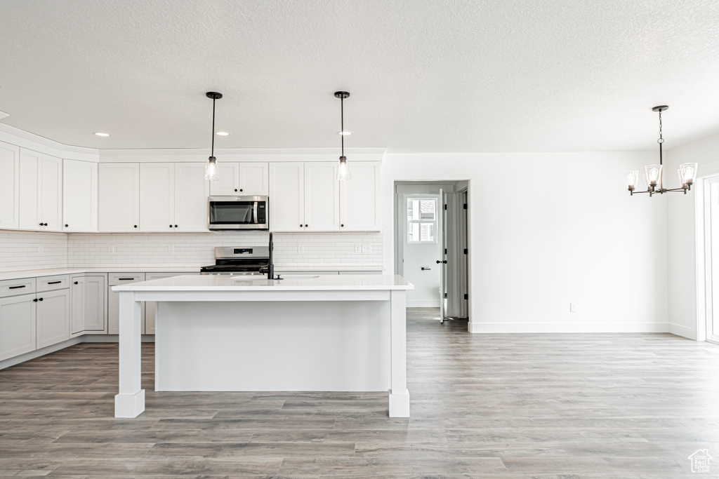 Kitchen with stainless steel appliances, backsplash, a chandelier, a center island with sink, and recessed lighting