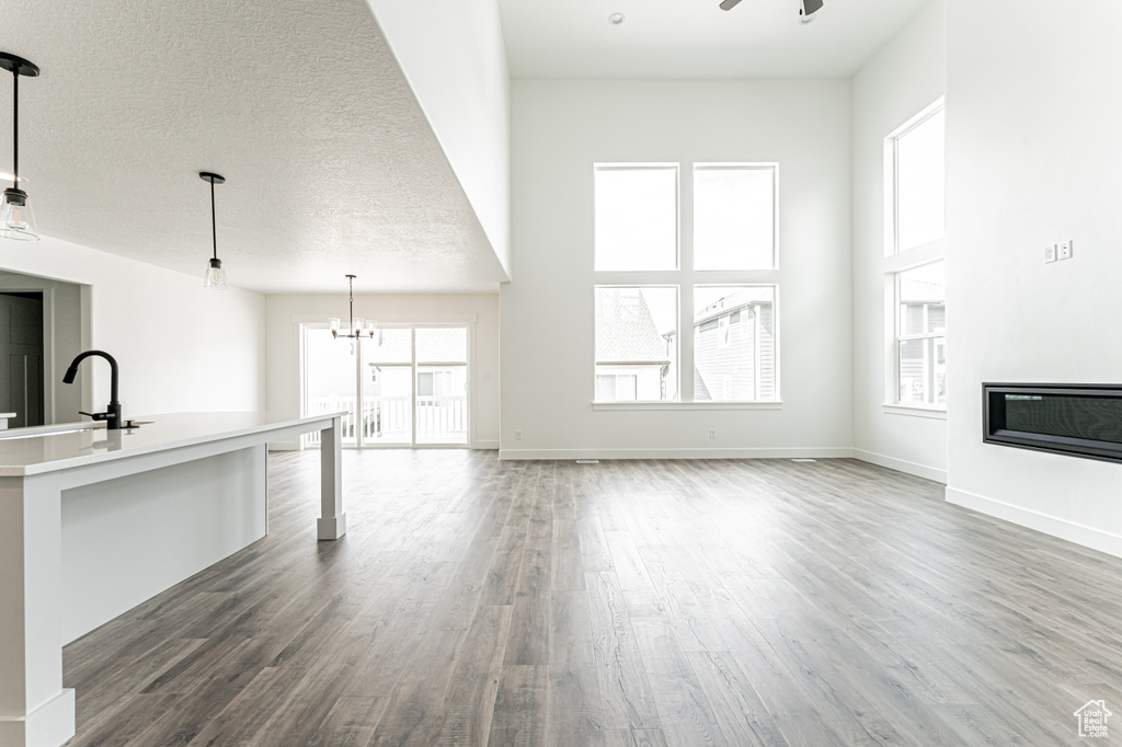 Unfurnished living room featuring dark wood finished floors, a ceiling fan, a chandelier, a glass covered fireplace, and a towering ceiling