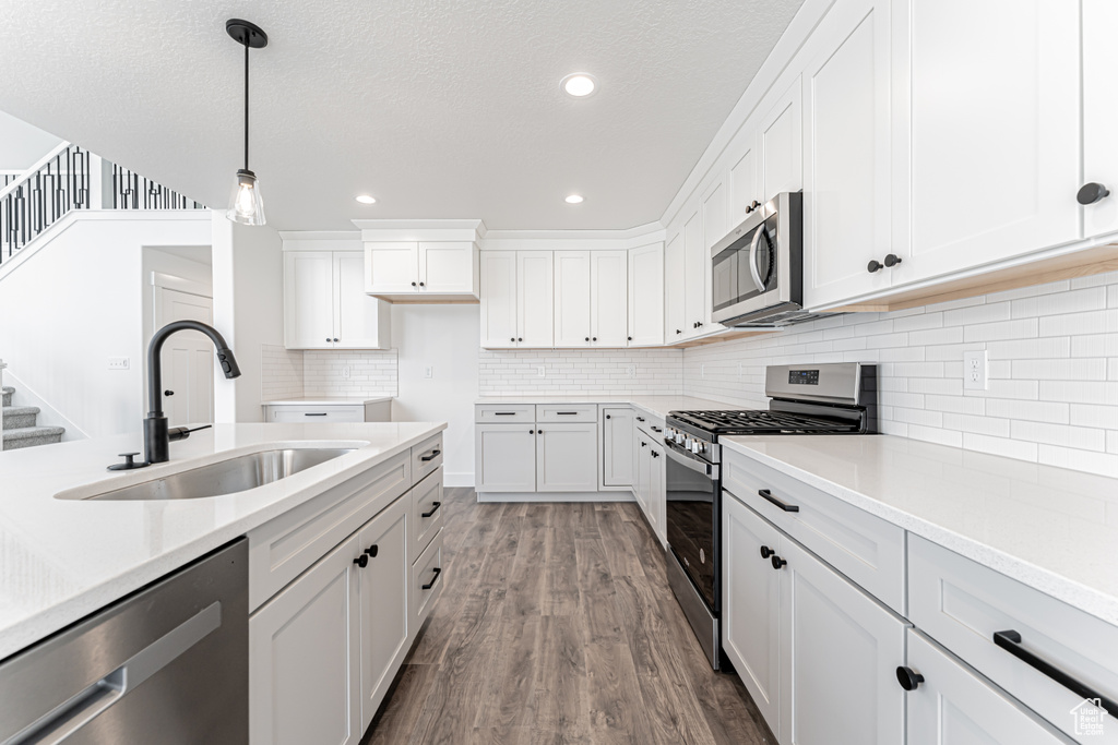 Kitchen with stainless steel appliances, dark wood finished floors, light countertops, hanging light fixtures, and white cabinetry