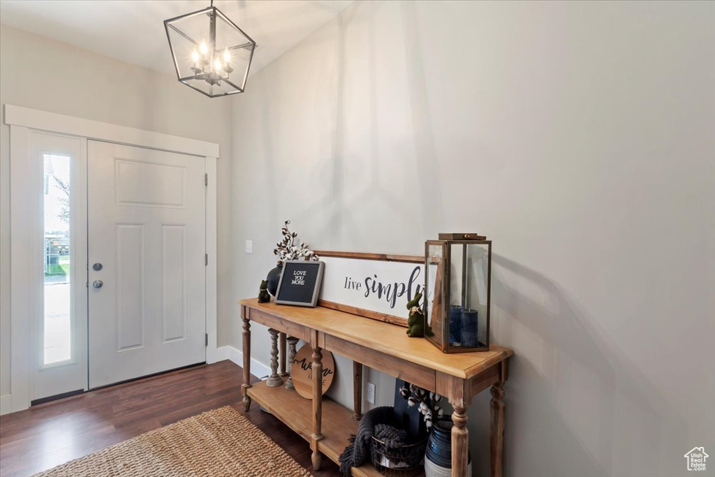 Entrance foyer with dark wood-style flooring, a notable chandelier, and baseboards
