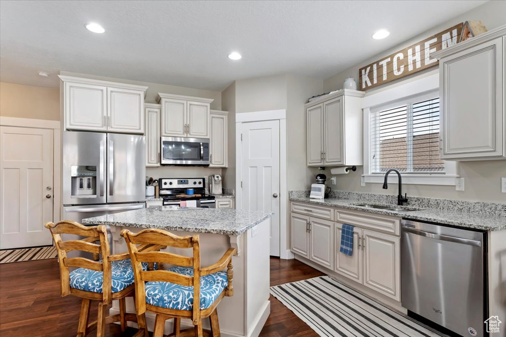 Kitchen featuring dark wood-style flooring, a kitchen breakfast bar, recessed lighting, appliances with stainless steel finishes, and a sink