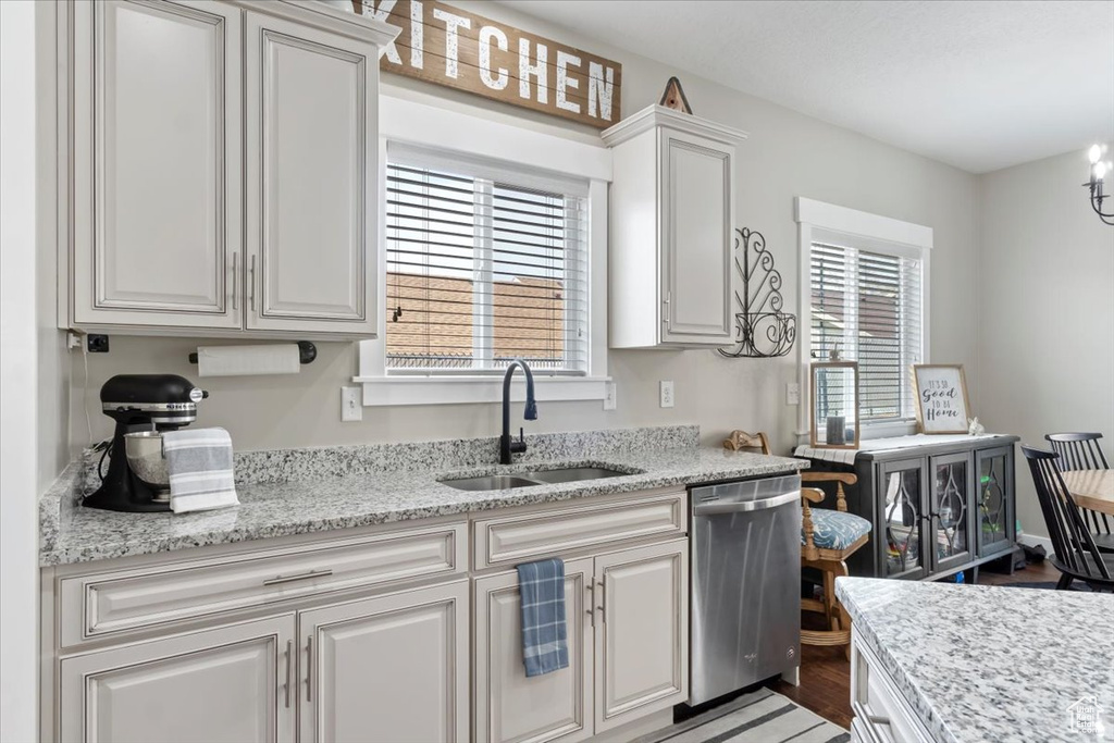 Kitchen featuring light stone counters, white cabinets, light wood-style floors, stainless steel dishwasher, and a sink