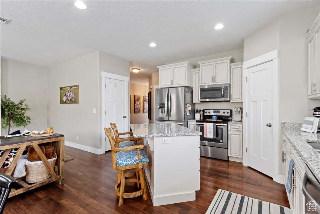 Kitchen featuring a kitchen island, dark wood-style flooring, a breakfast bar, and appliances with stainless steel finishes