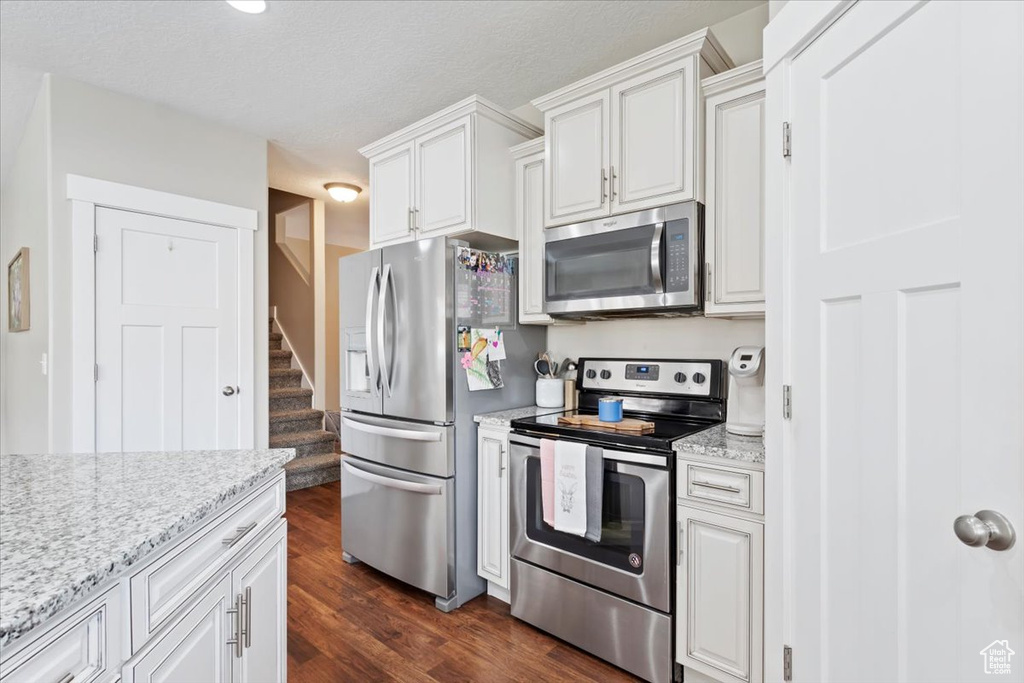 Kitchen with light stone counters, dark wood-style flooring, white cabinets, and stainless steel appliances