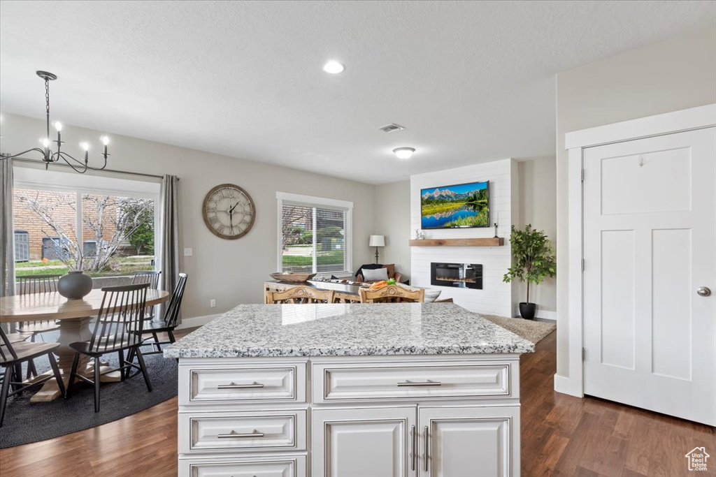 Kitchen with light stone counters, a notable chandelier, dark wood finished floors, and a glass covered fireplace