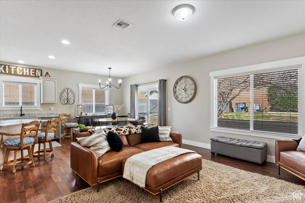 Living area with dark wood-style flooring, visible vents, baseboards, and an inviting chandelier