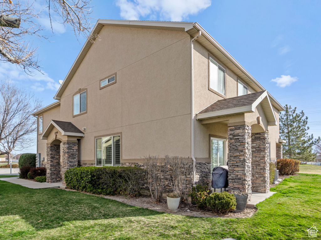 View of side of property with a yard, stucco siding, and stone siding