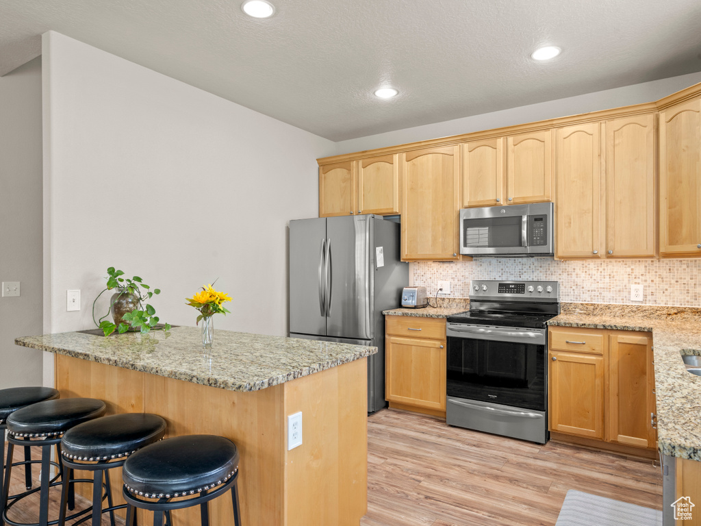 Kitchen featuring stainless steel appliances, tasteful backsplash, light wood-type flooring, and a kitchen bar