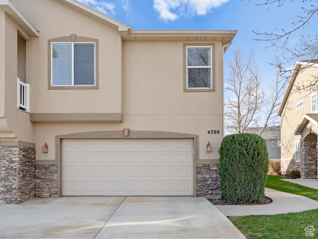 View of front of property with an attached garage, stone siding, driveway, and stucco siding