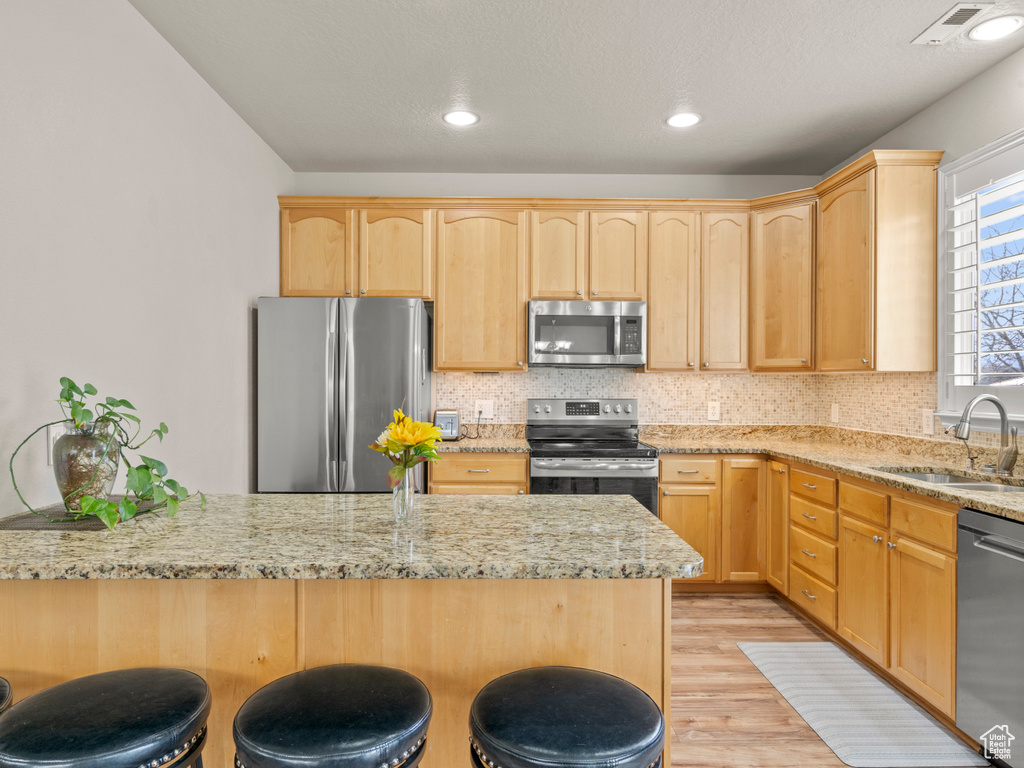 Kitchen with a sink, a kitchen breakfast bar, light brown cabinets, and stainless steel appliances