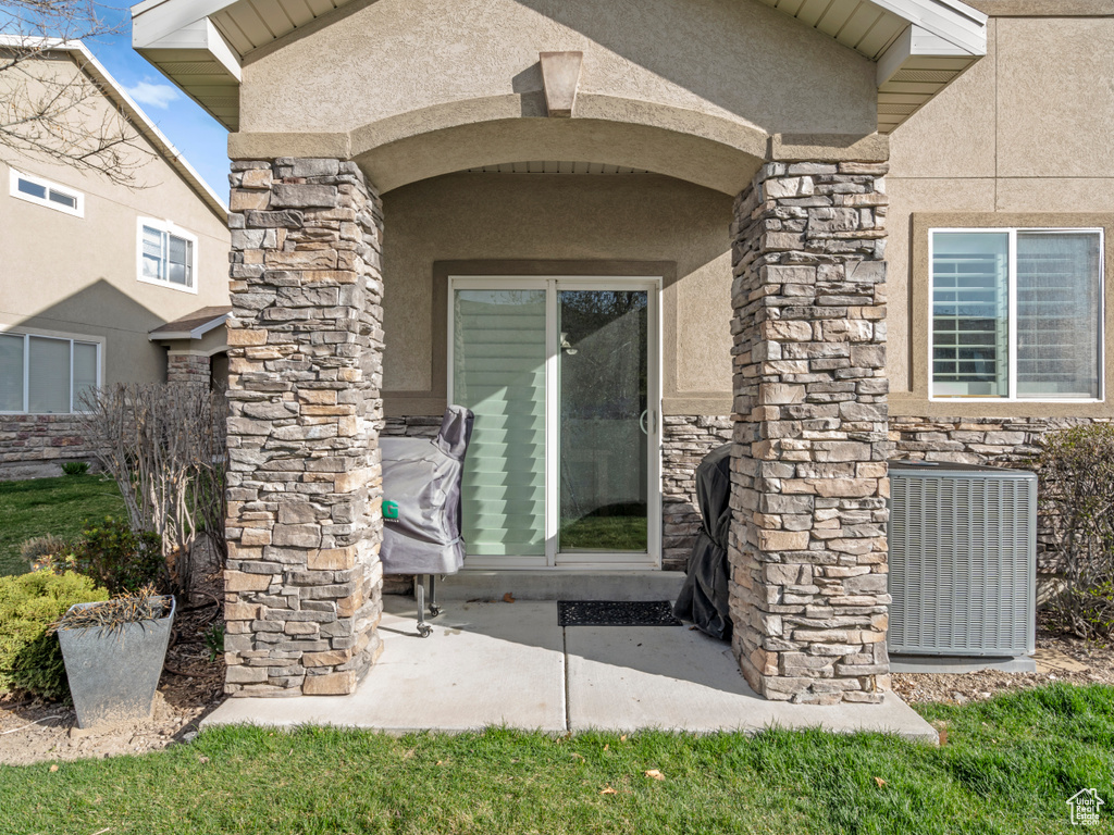Entrance to property with stucco siding, stone siding, and cooling unit