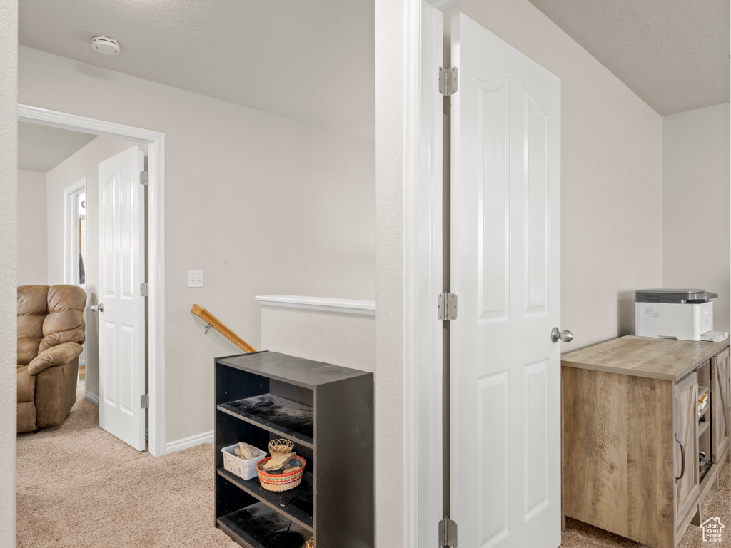 Hall with an upstairs landing, light colored carpet, and baseboards