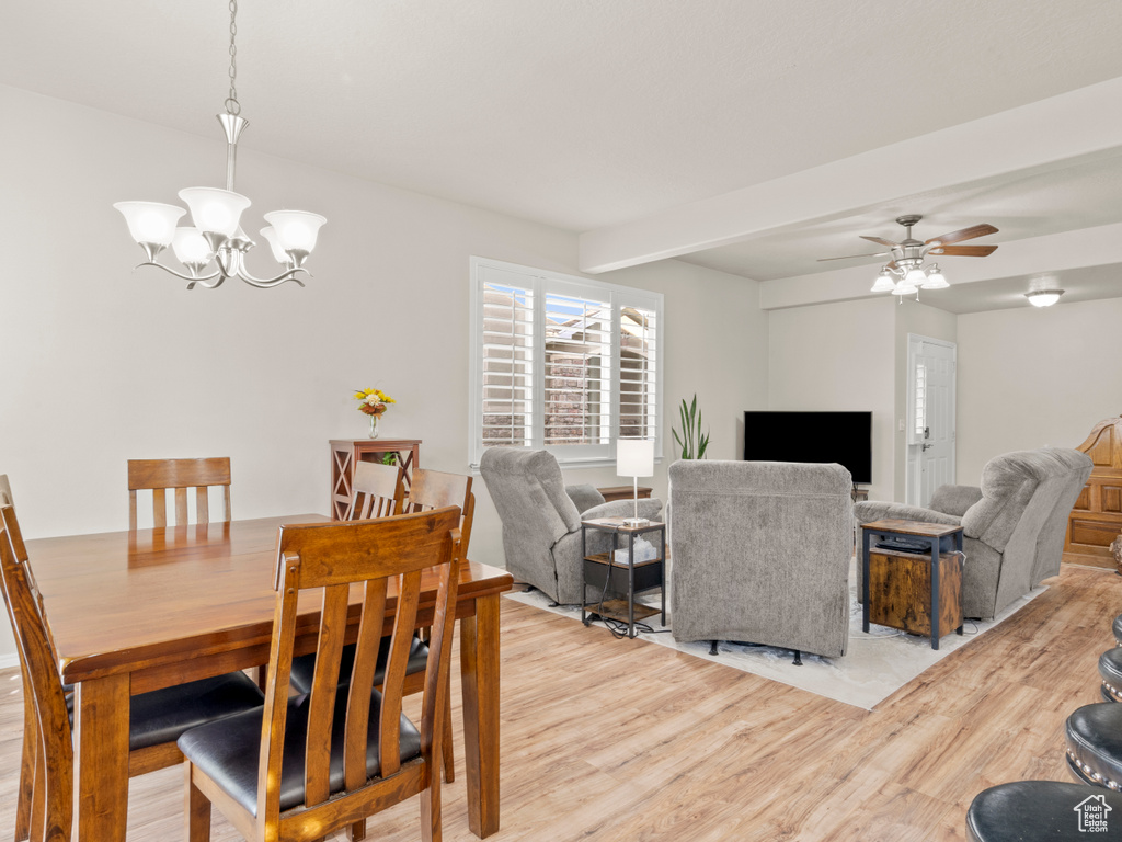 Dining space with beam ceiling, light wood finished floors, and ceiling fan with notable chandelier
