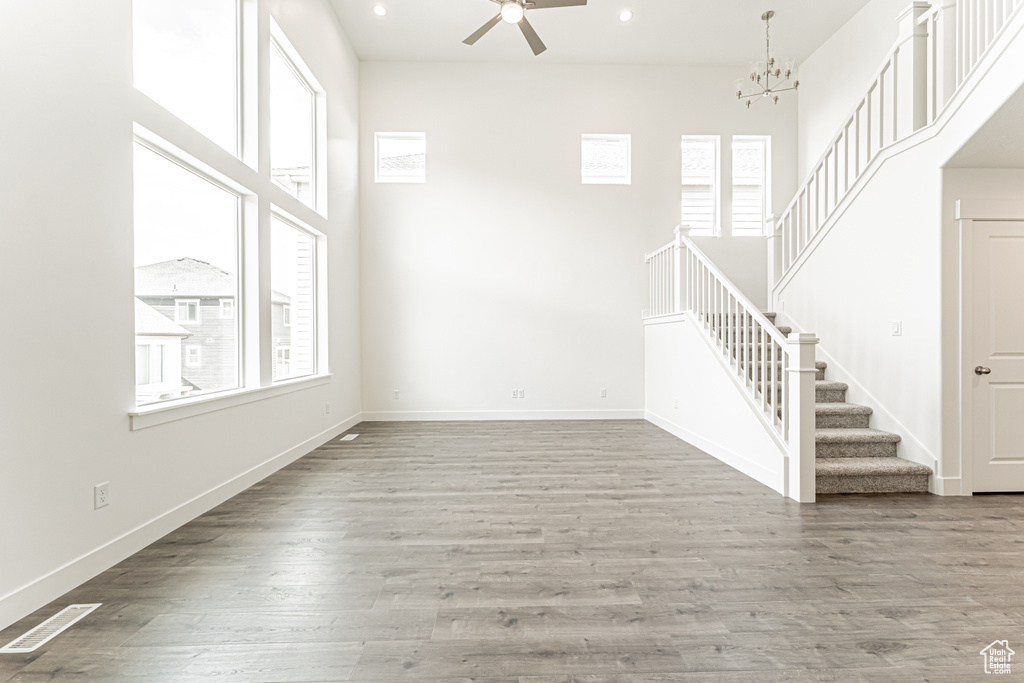 Unfurnished living room with healthy amount of natural light, stairway, a ceiling fan, recessed lighting, and a chandelier