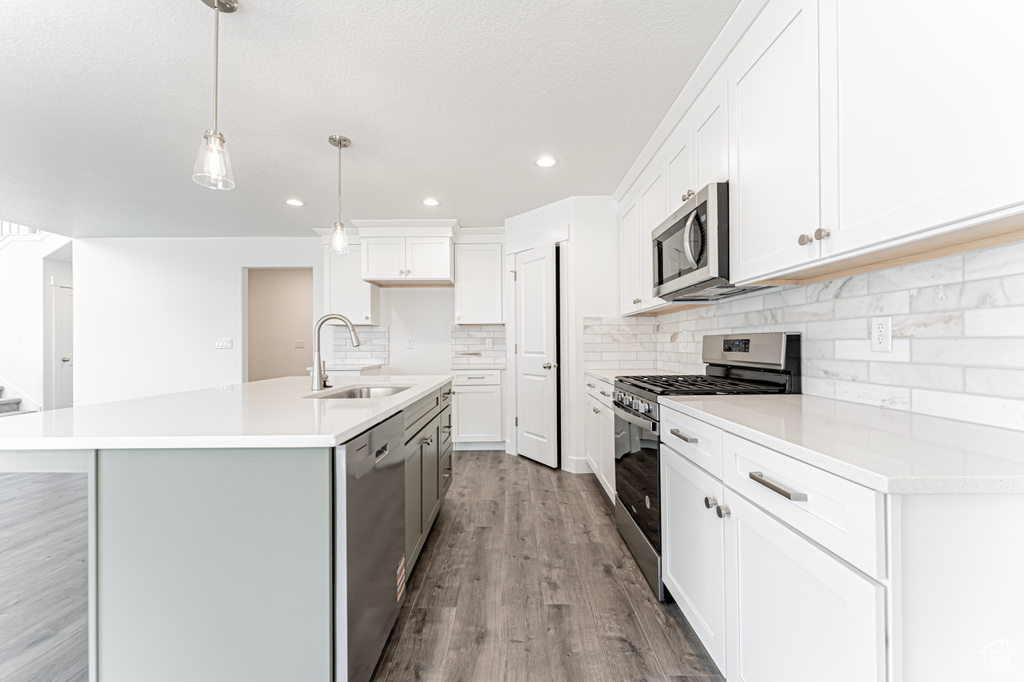 Kitchen with appliances with stainless steel finishes, wood finished floors, backsplash, a center island with sink, and recessed lighting