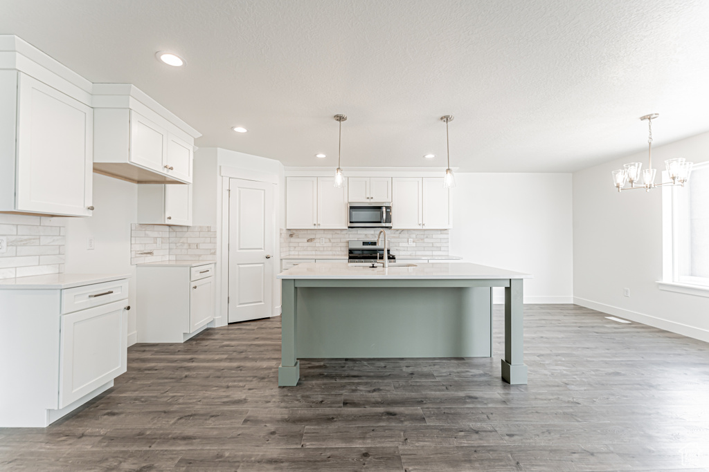 Kitchen featuring stainless steel microwave, backsplash, dark wood-type flooring, recessed lighting, and a kitchen island with sink