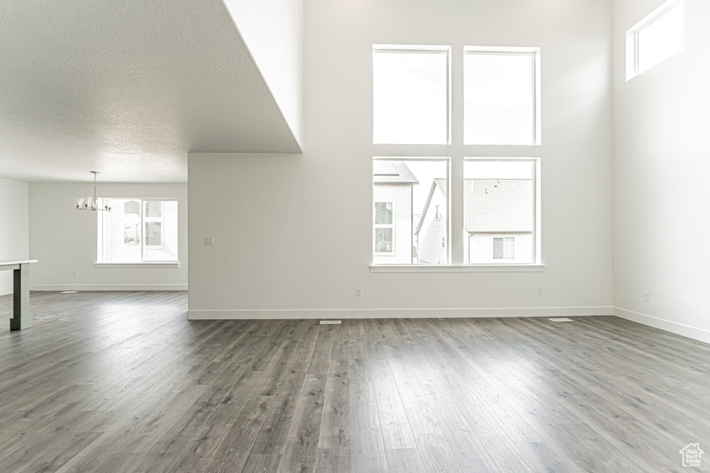 Unfurnished living room with a chandelier, wood finished floors, and a textured ceiling