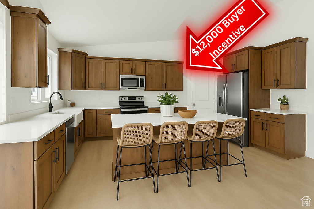 Kitchen with stainless steel appliances, a kitchen island, vaulted ceiling, a breakfast bar, and a sink