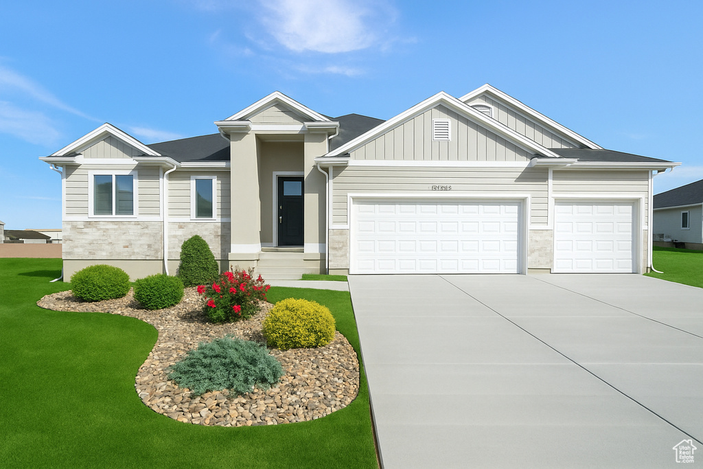 View of front of property featuring an attached garage, stone siding, board and batten siding, a front yard, and driveway