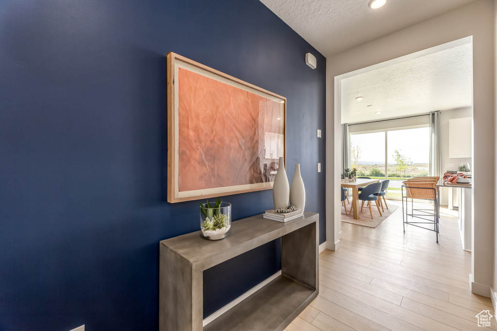 Hallway featuring light wood-style floors, a textured ceiling, and baseboards