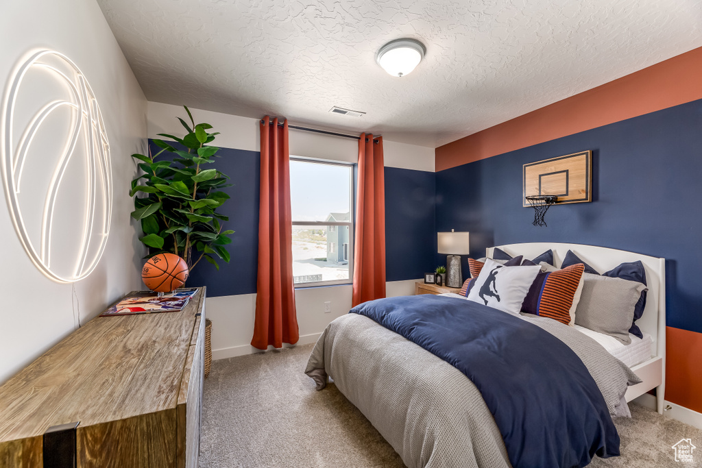 Bedroom featuring carpet flooring, visible vents, a textured ceiling, and baseboards