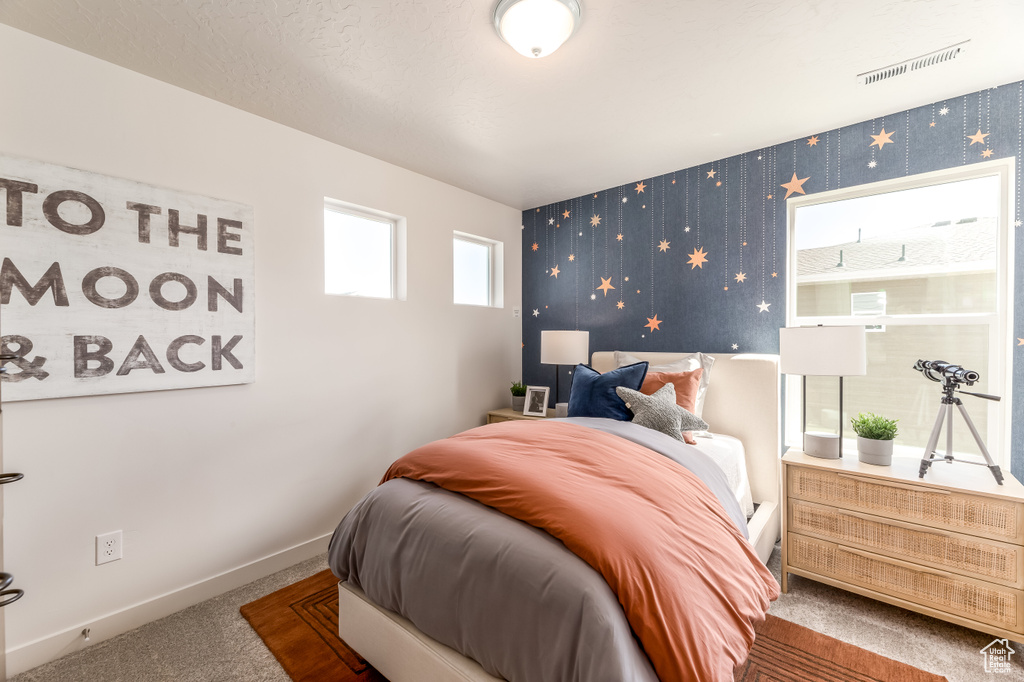 Carpeted bedroom with visible vents, baseboards, wallpapered walls, and an accent wall