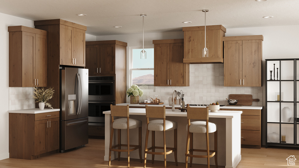 Kitchen with light countertops, appliances with stainless steel finishes, a kitchen bar, light wood finished floors, and backsplash