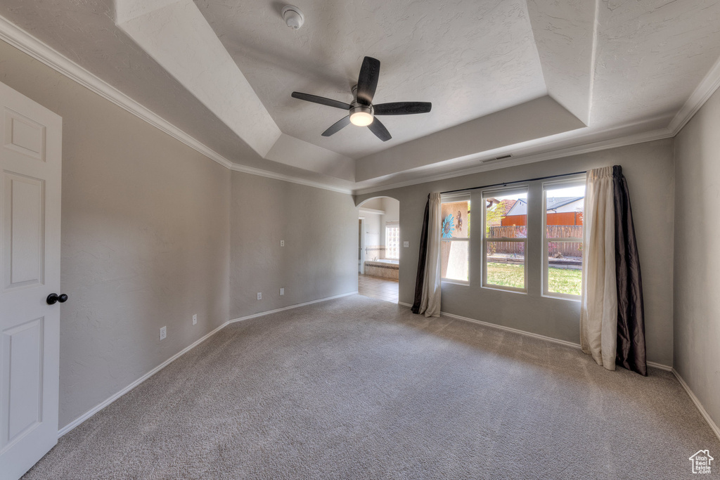 Carpeted spare room featuring baseboards, a raised ceiling, arched walkways, ornamental molding, and ceiling fan