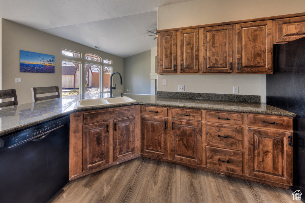 Kitchen with a sink, dark countertops, black appliances, vaulted ceiling, and wood finished floors