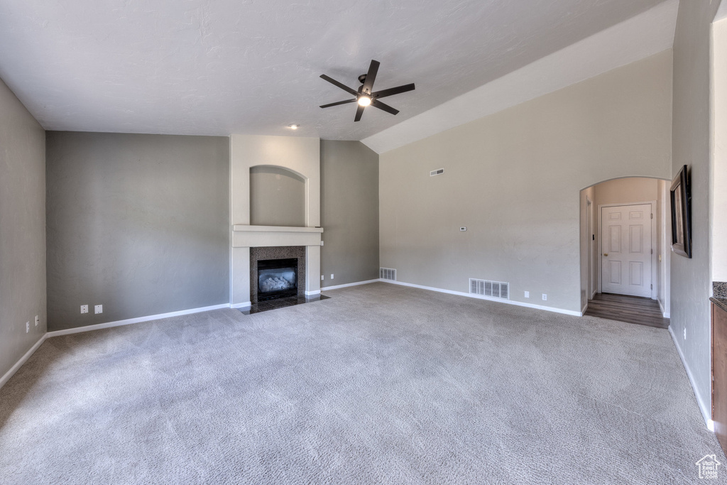 Unfurnished living room featuring carpet flooring, a fireplace with flush hearth, visible vents, and a ceiling fan