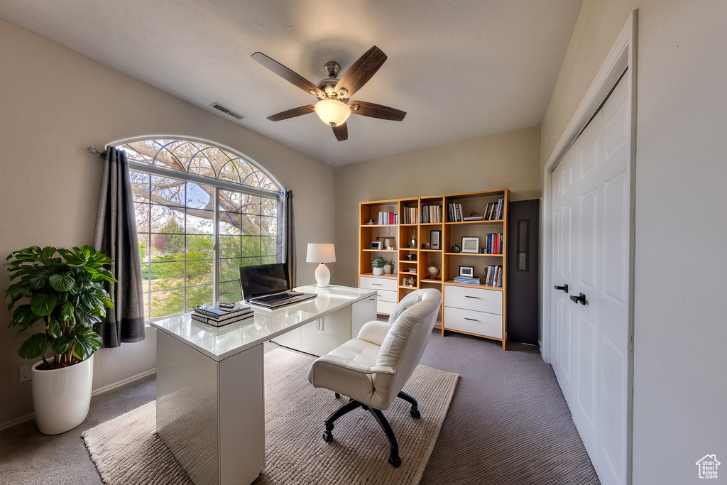 Home office with dark carpet, ceiling fan, and visible vents