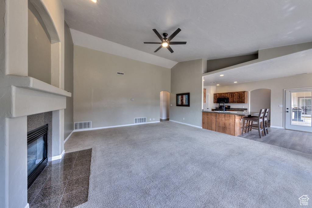 Unfurnished living room with ceiling fan, arched walkways, visible vents, a tile fireplace, and baseboards