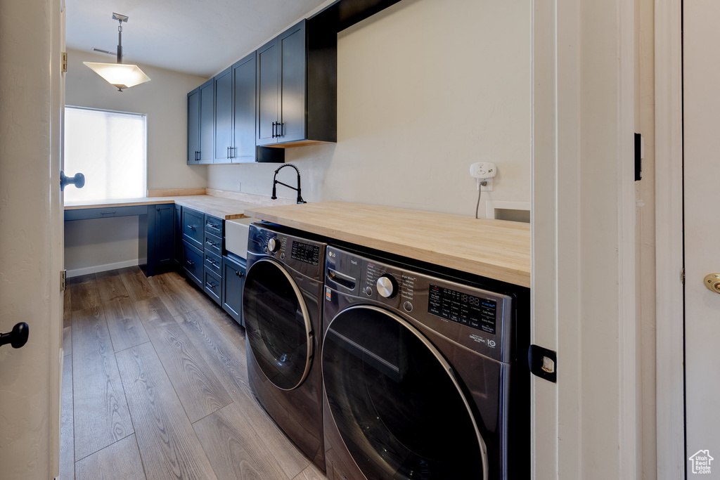 Washroom featuring wood finished floors, washing machine and clothes dryer, a sink, and cabinet space