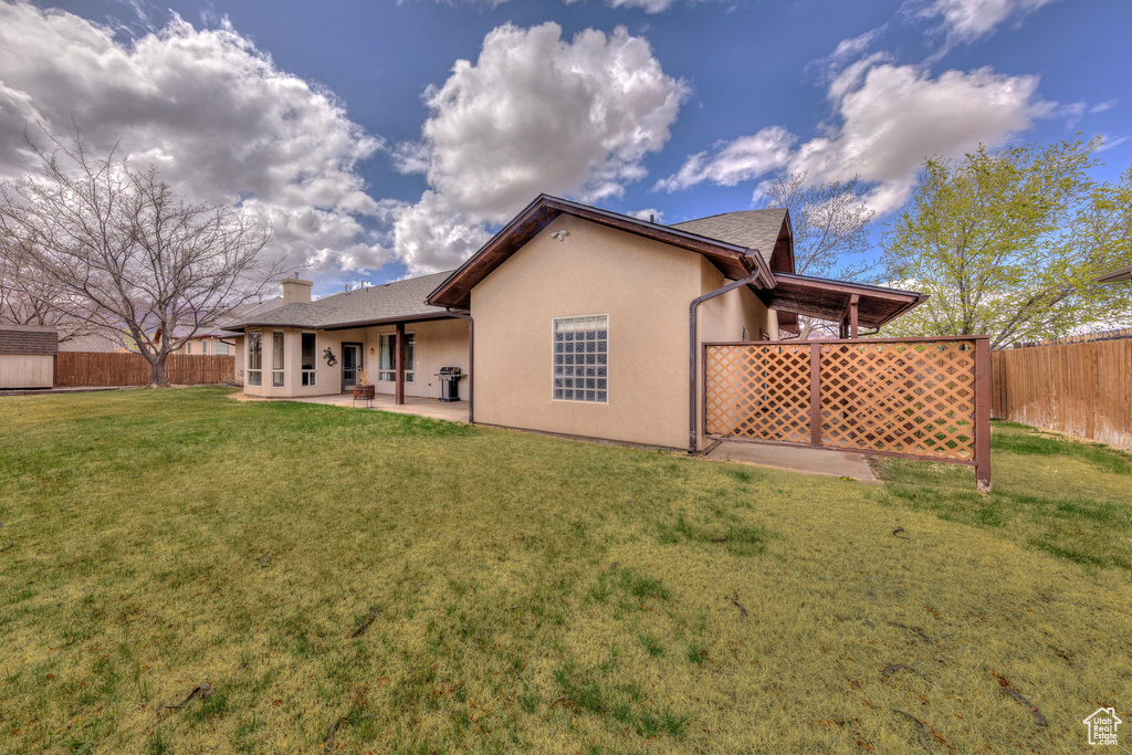 Back of house with stucco siding, a chimney, a patio area, a fenced backyard, and a yard