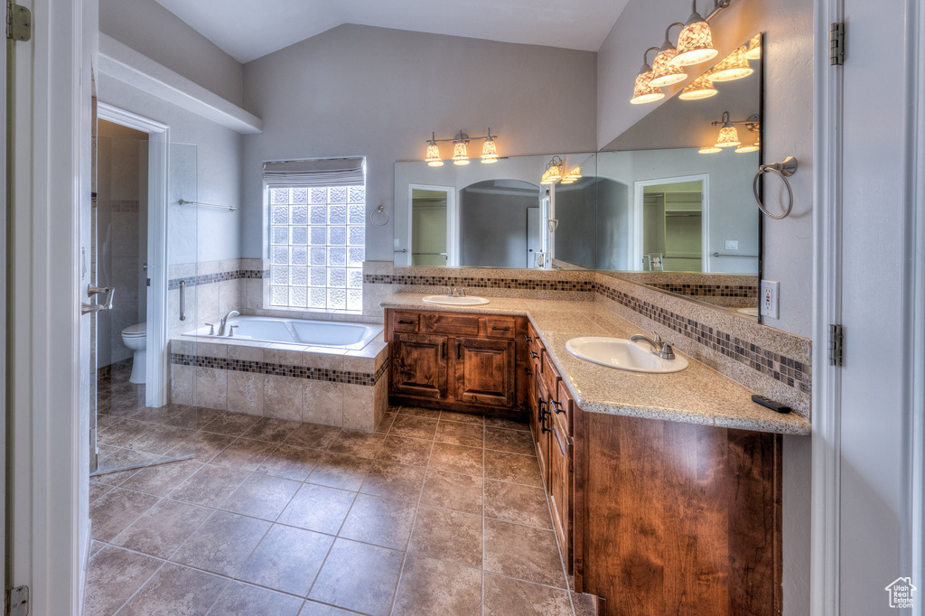 Bathroom with double vanity, toilet, a bath, lofted ceiling, and a sink