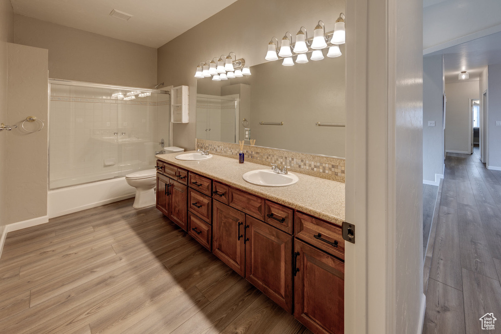 Full bath featuring toilet, wood finished floors, double vanity, and a sink