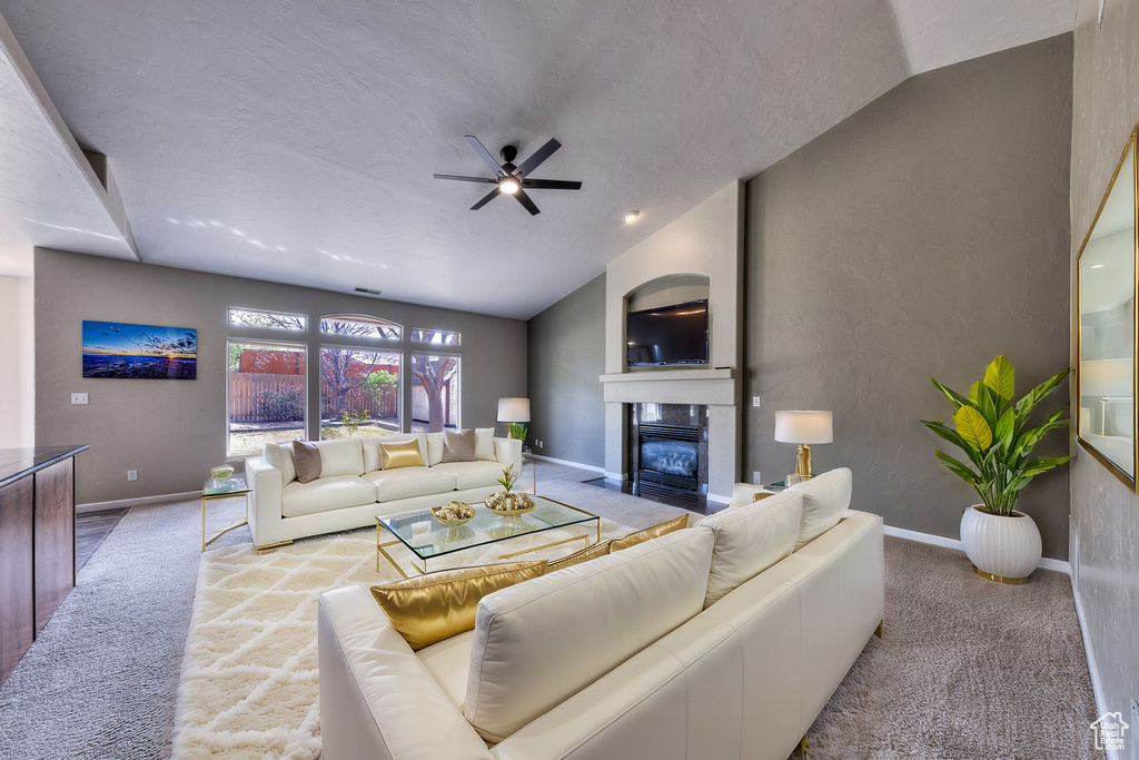 Living room featuring a fireplace with flush hearth, ceiling fan, lofted ceiling, and carpet floors