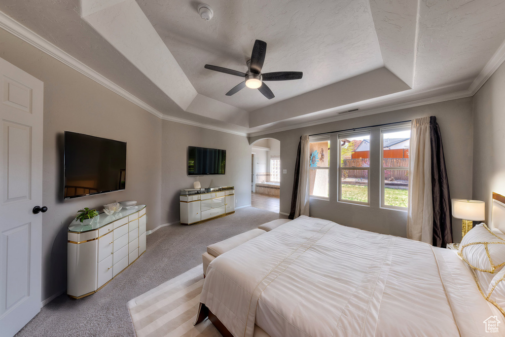Bedroom with baseboards, a raised ceiling, arched walkways, ornamental molding, and light carpet
