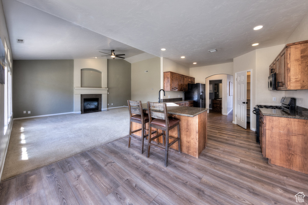 Kitchen featuring stainless steel microwave, gas range oven, a ceiling fan, black refrigerator with ice dispenser, and arched walkways