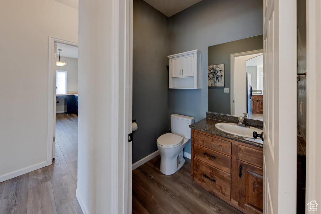 Half bath featuring toilet, vanity, wood finished floors, and baseboards