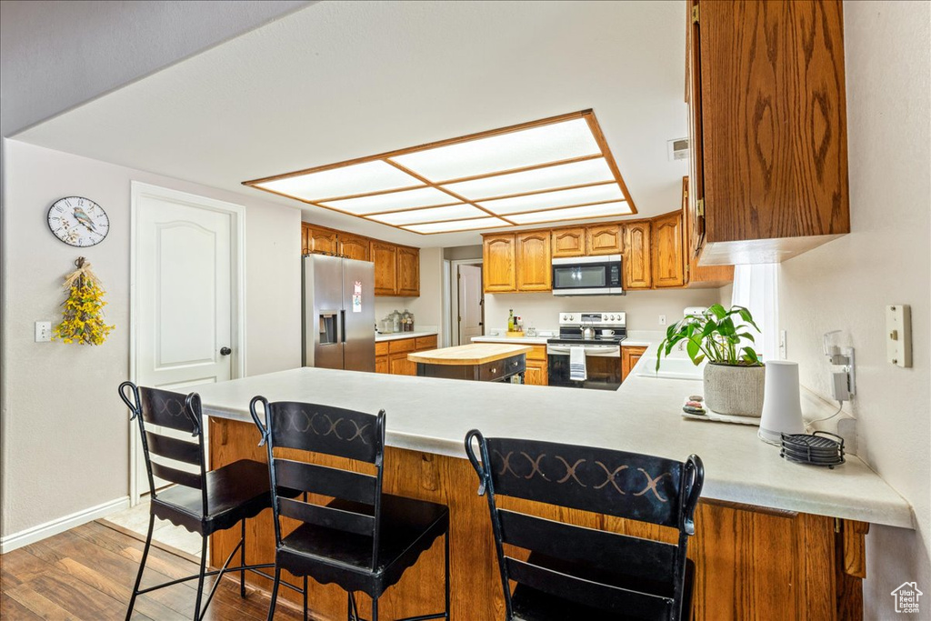 Kitchen with a peninsula, light countertops, brown cabinets, stainless steel appliances, and wood finished floors