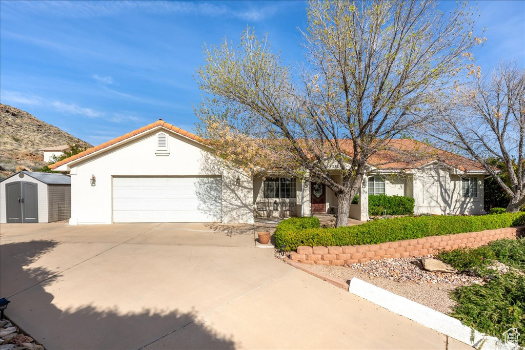 Ranch-style house with concrete driveway, stucco siding, a porch, a storage shed, and a garage